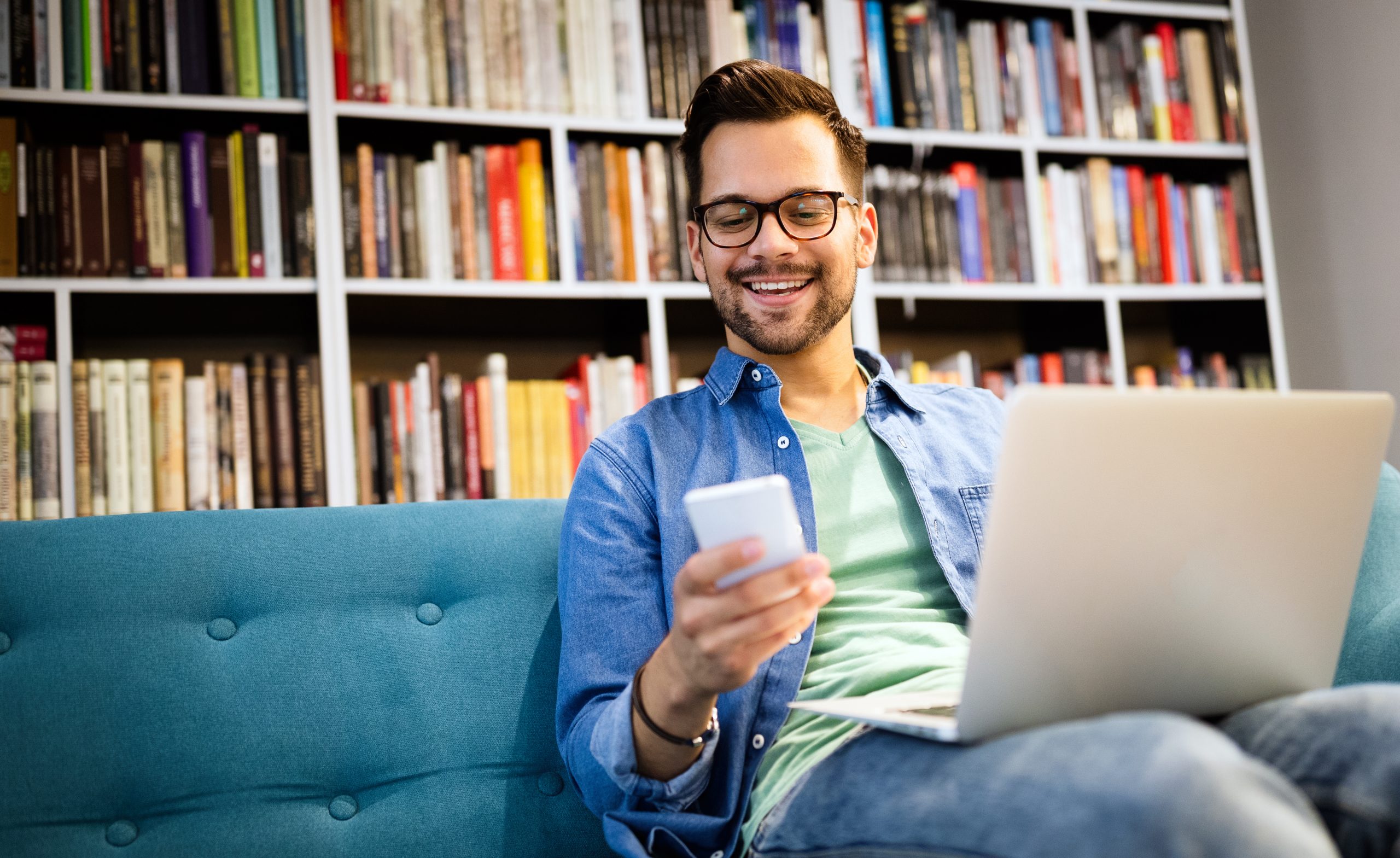 Estudante na biblioteca falando no celular e trabalhando no laptop