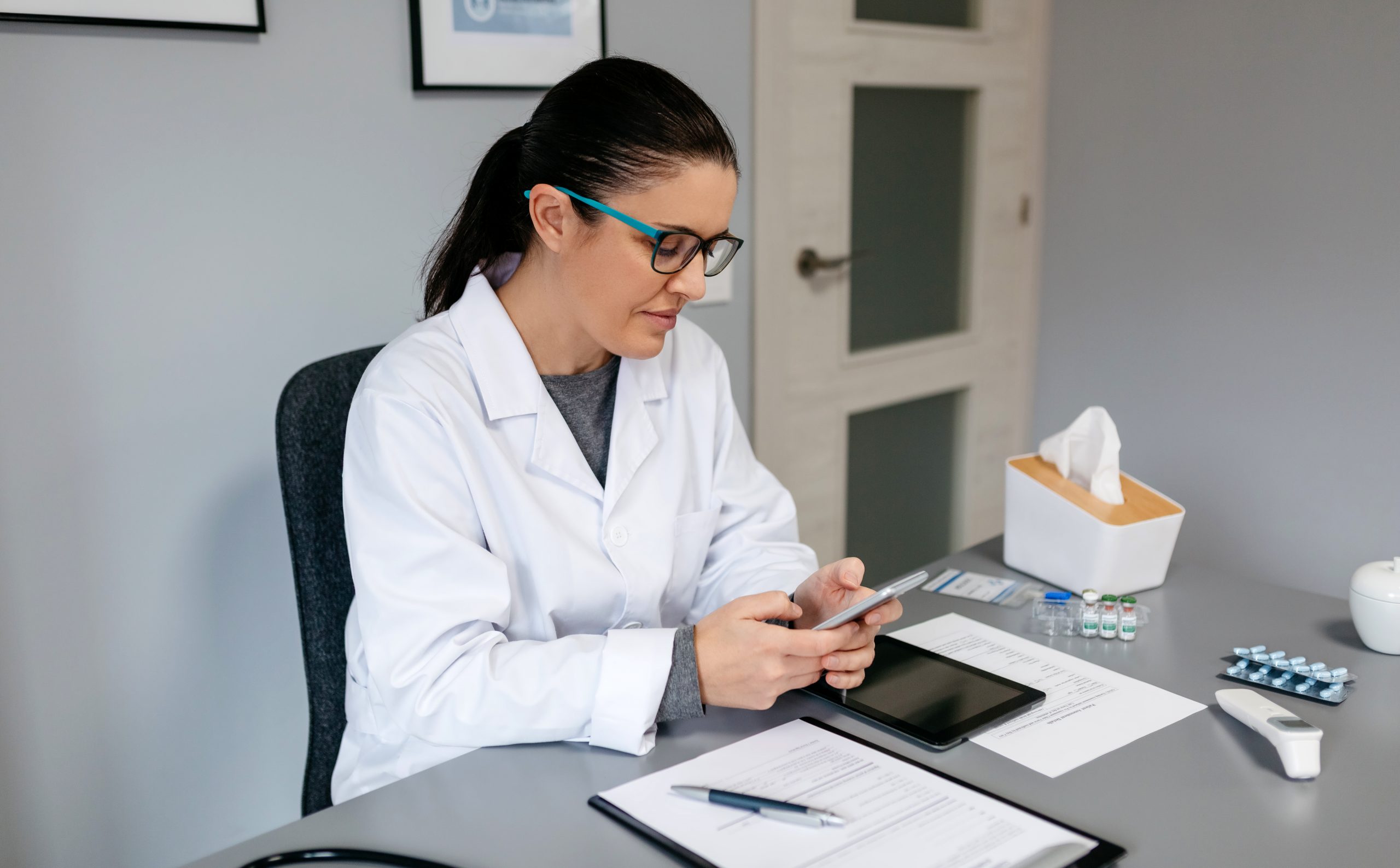 Médica usando celular enquanto trabalha em seu consultório